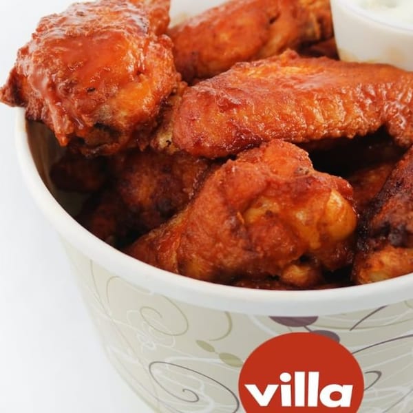 A bucket of Villa Pizza's buffalo wings, coated in red sauce, with a side of ranch.